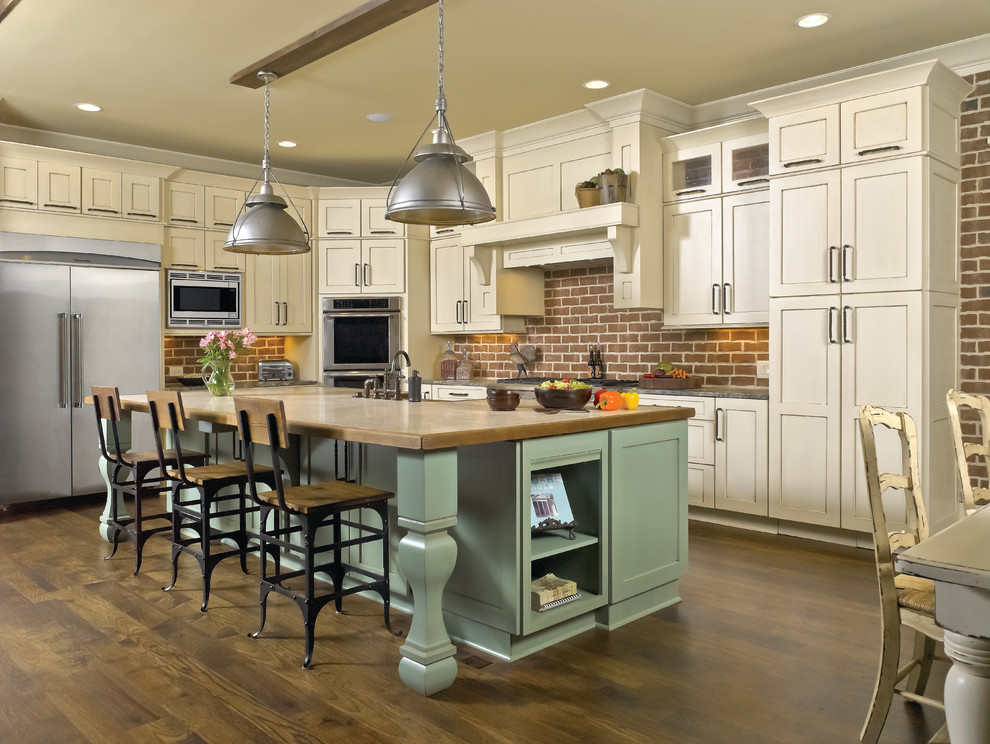 Inspiration for a mid-sized country u-shaped open plan kitchen in Chicago with a farmhouse sink, shaker cabinets, brick splashback, stainless steel appliances, dark hardwood floors, brown floor, beige cabinets, wood benchtops, red splashback and with island.