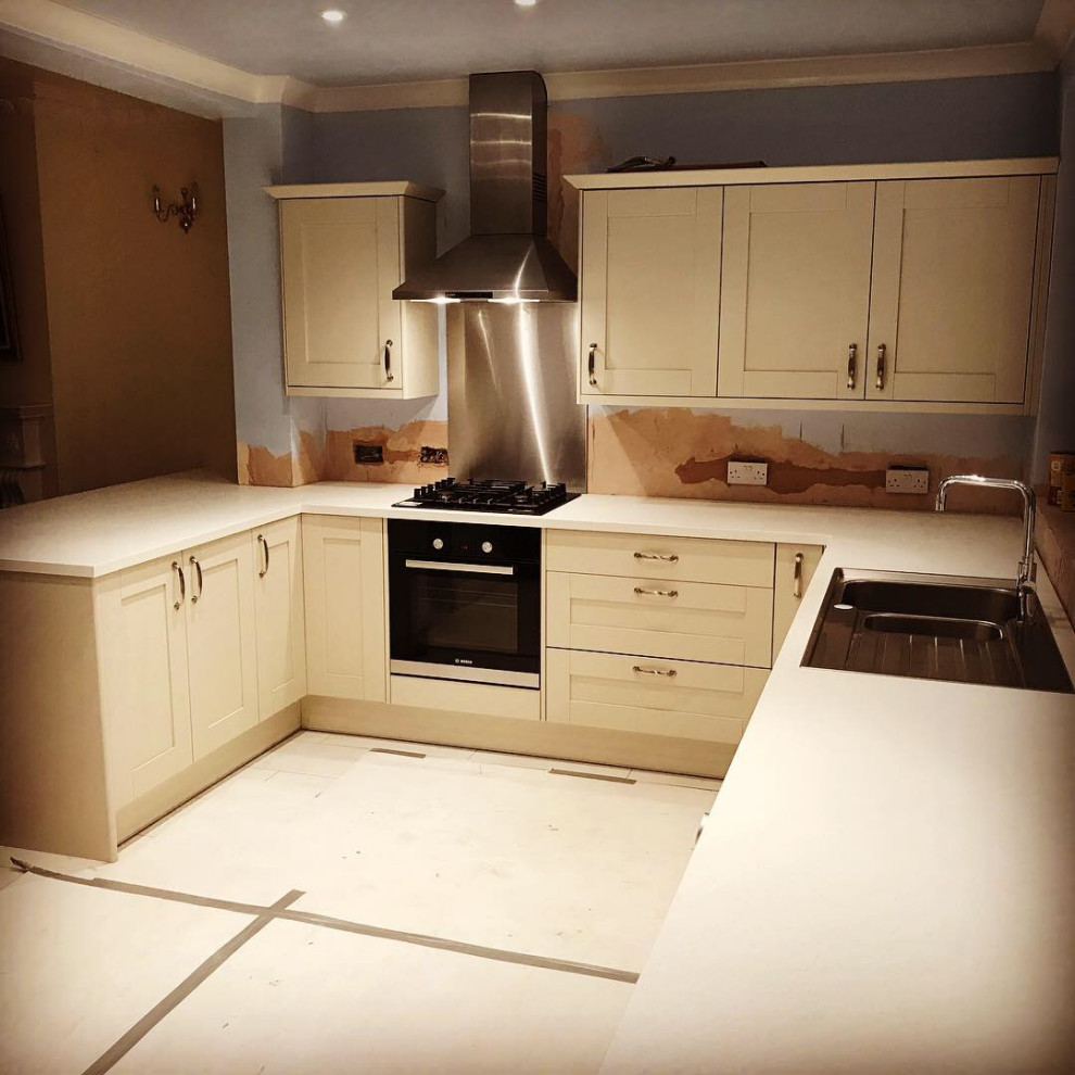 Large victorian u-shaped open plan kitchen in London with a double-bowl sink, shaker cabinets, white cabinets, laminate countertops, red splashback, ceramic splashback, integrated appliances, porcelain flooring, multi-coloured floors, white worktops and feature lighting.