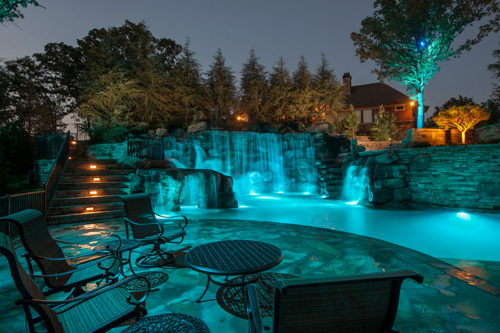 This is an example of an expansive country backyard custom-shaped natural pool in Oklahoma City with a water feature and natural stone pavers.