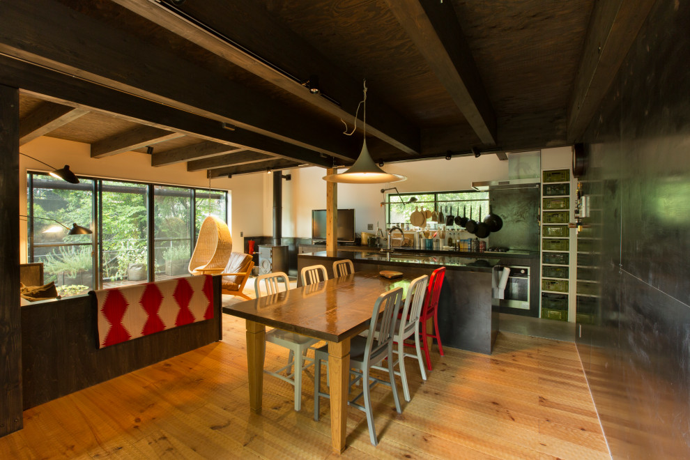 Cette photo montre une grande salle à manger moderne avec un mur blanc, un sol en bois brun, un poêle à bois, un manteau de cheminée en métal, poutres apparentes et du lambris de bois.