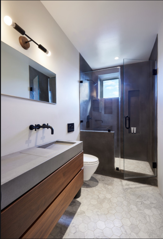 Photo of a mid-sized contemporary master bathroom in New York with flat-panel cabinets, medium wood cabinets, an alcove shower, a wall-mount toilet, black tile, stone slab, white walls, marble floors, an integrated sink, concrete benchtops, grey floor, a hinged shower door and grey benchtops.