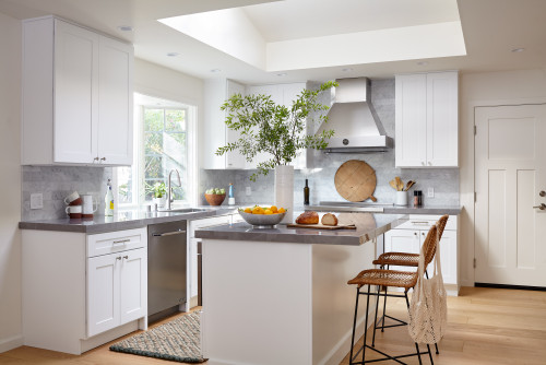 RTA cabinets in a bright white shaker kitchen with gray stone countertops, stainless appliances, and a peninsula breakfast bar.