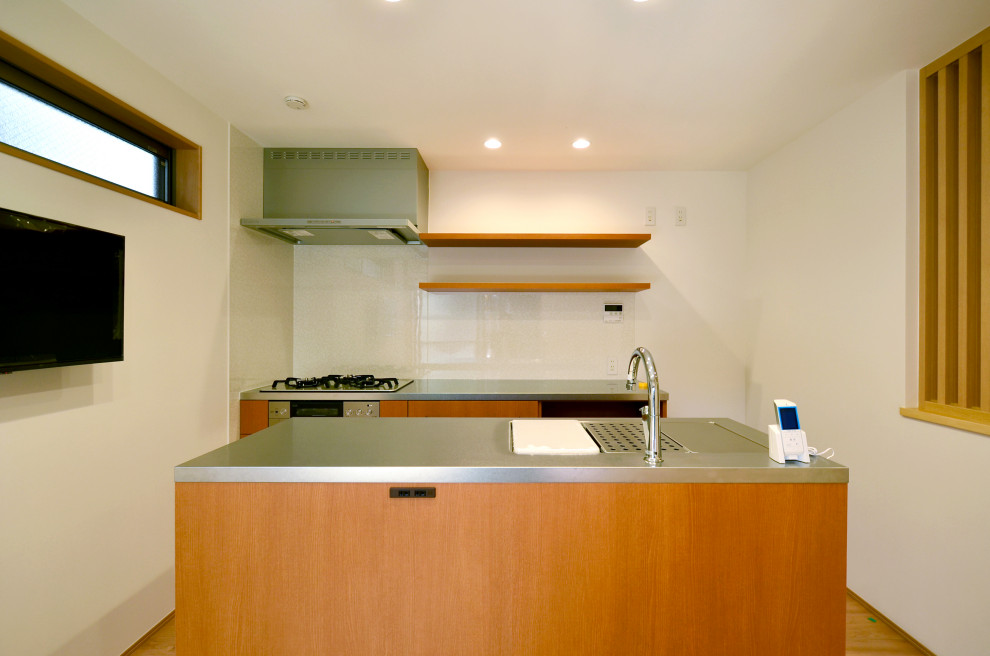 Small country galley kitchen/diner in Tokyo with a submerged sink, flat-panel cabinets, medium wood cabinets, stainless steel worktops, stainless steel appliances, medium hardwood flooring, an island, brown floors, grey worktops and a wallpapered ceiling.