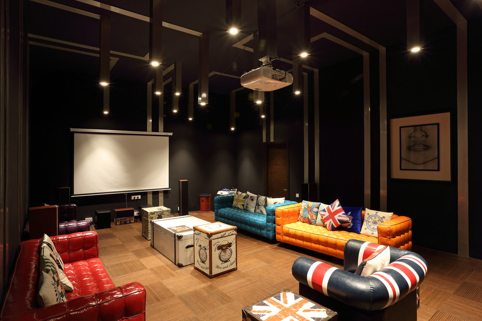 This is an example of a large eclectic enclosed home theatre in Pune with medium hardwood floors, brown floor, black walls and a projector screen.