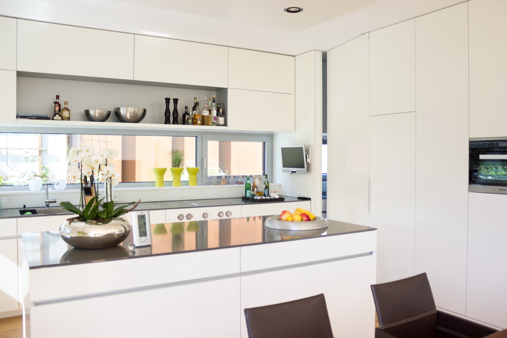 Kleine Moderne Wohnküche in L-Form mit Einbauwaschbecken, flächenbündigen Schrankfronten, weißen Schränken, Küchenrückwand in Braun, Rückwand aus Holz, Küchengeräten aus Edelstahl, Halbinsel, grauem Boden und weißer Arbeitsplatte in Sonstige