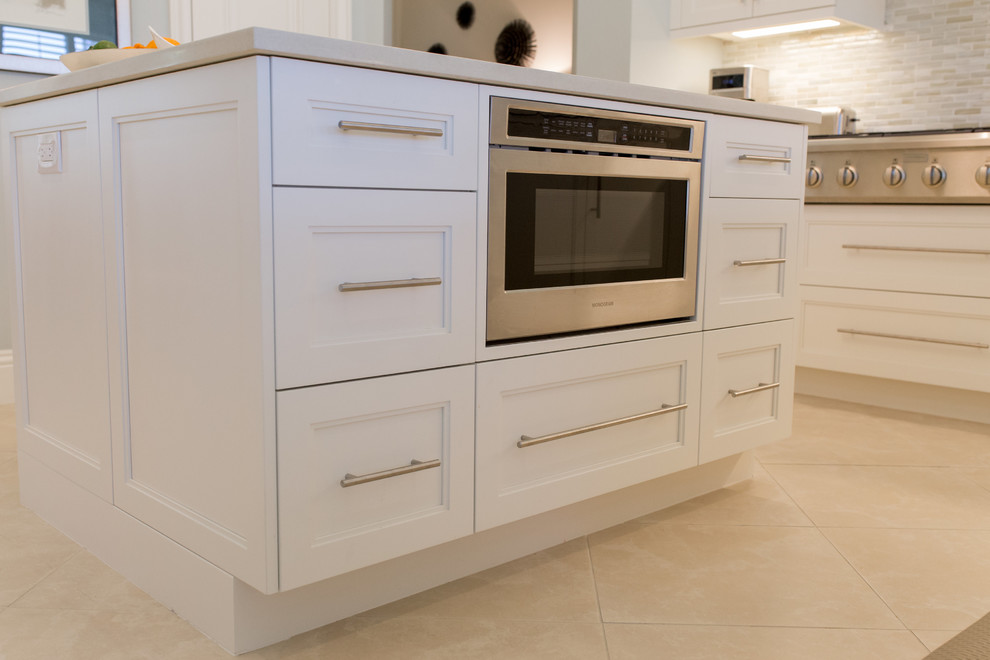 This is an example of a large beach style l-shaped open plan kitchen in Miami with an undermount sink, recessed-panel cabinets, white cabinets, quartz benchtops, beige splashback, matchstick tile splashback, stainless steel appliances, ceramic floors, with island and beige floor.
