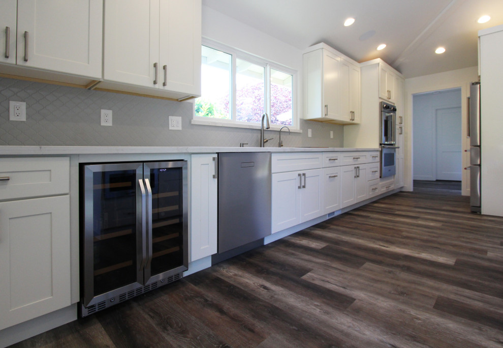 Open concept kitchen - large transitional single-wall vinyl floor and brown floor open concept kitchen idea with an undermount sink, shaker cabinets, white cabinets, quartz countertops, gray backsplash, ceramic backsplash, stainless steel appliances, an island and white countertops