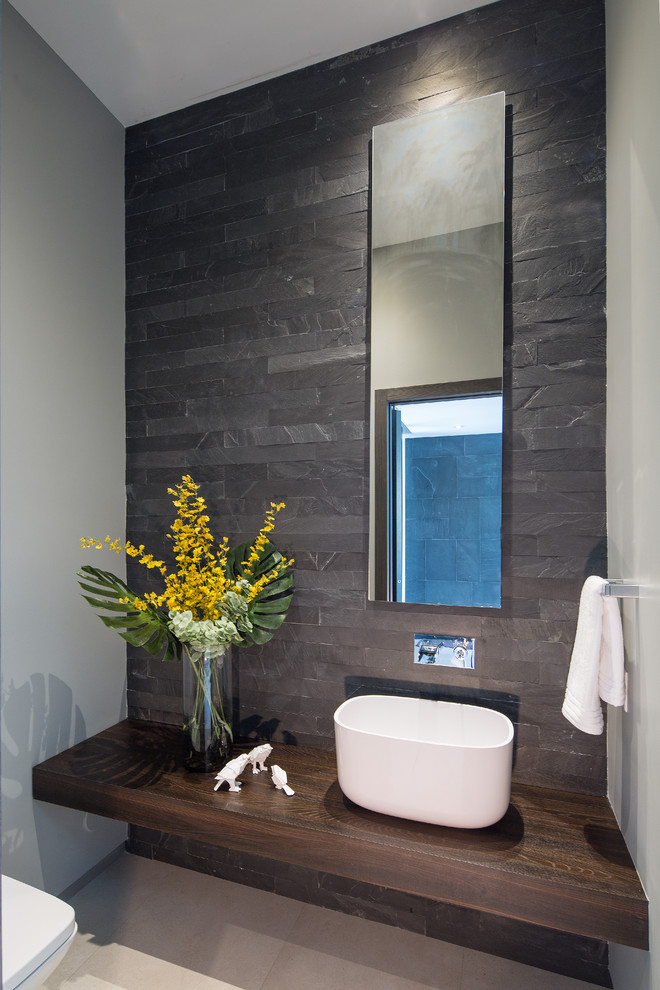 This is an example of a small contemporary powder room in Miami with slate, gray tile, grey walls, ceramic floors, a vessel sink, beige floor and brown benchtops.