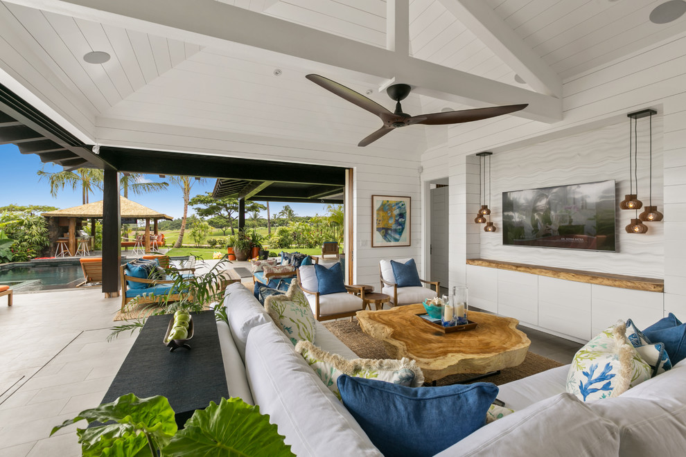 This is an example of a large tropical open concept living room in Hawaii with white walls, ceramic floors, no fireplace, grey floor and a wall-mounted tv.