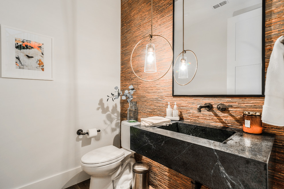 This is an example of a small contemporary powder room in Dallas with a two-piece toilet, multi-coloured tile, orange tile, matchstick tile, white walls, an integrated sink, black benchtops, open cabinets and black cabinets.