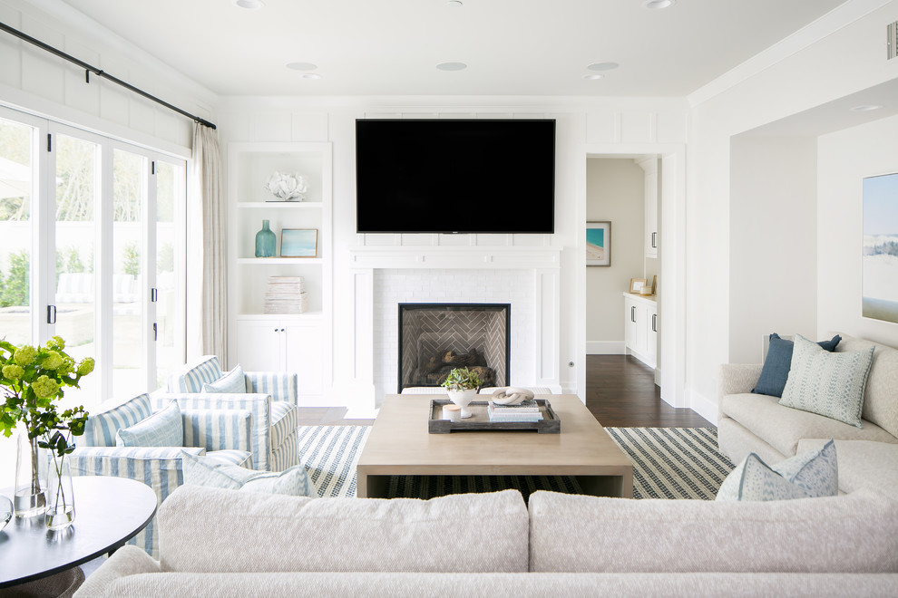 Beach style living room in Orange County with white walls, dark hardwood floors, a standard fireplace, a tile fireplace surround, a wall-mounted tv and brown floor.
