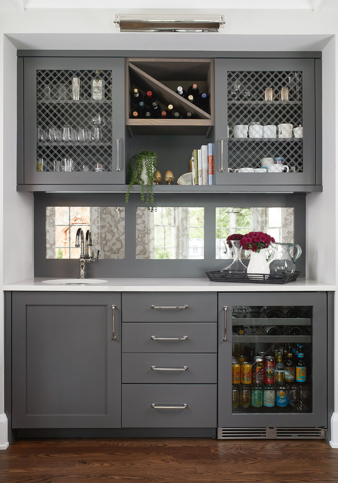 This is an example of a transitional single-wall wet bar in Grand Rapids with an undermount sink, grey cabinets, mirror splashback, dark hardwood floors, brown floor and white benchtop.