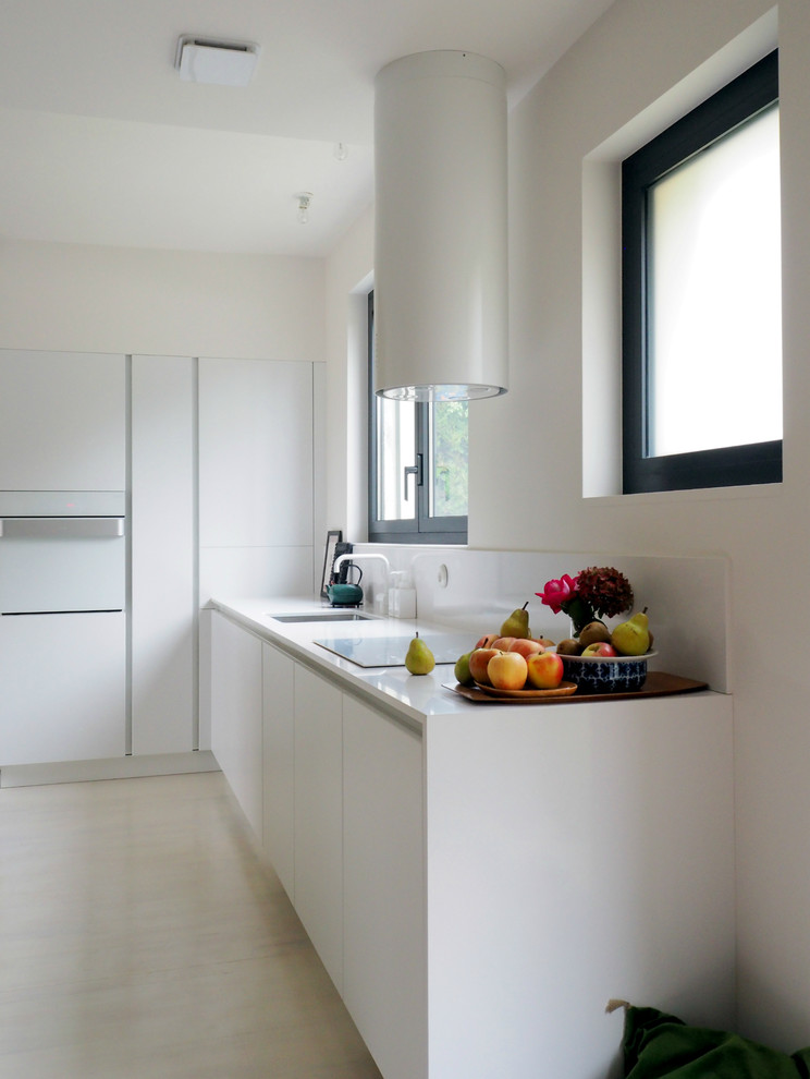 Design ideas for a mid-sized contemporary l-shaped open plan kitchen in Toulouse with an undermount sink, flat-panel cabinets, white cabinets, quartz benchtops, white splashback, glass sheet splashback, white appliances and no island.