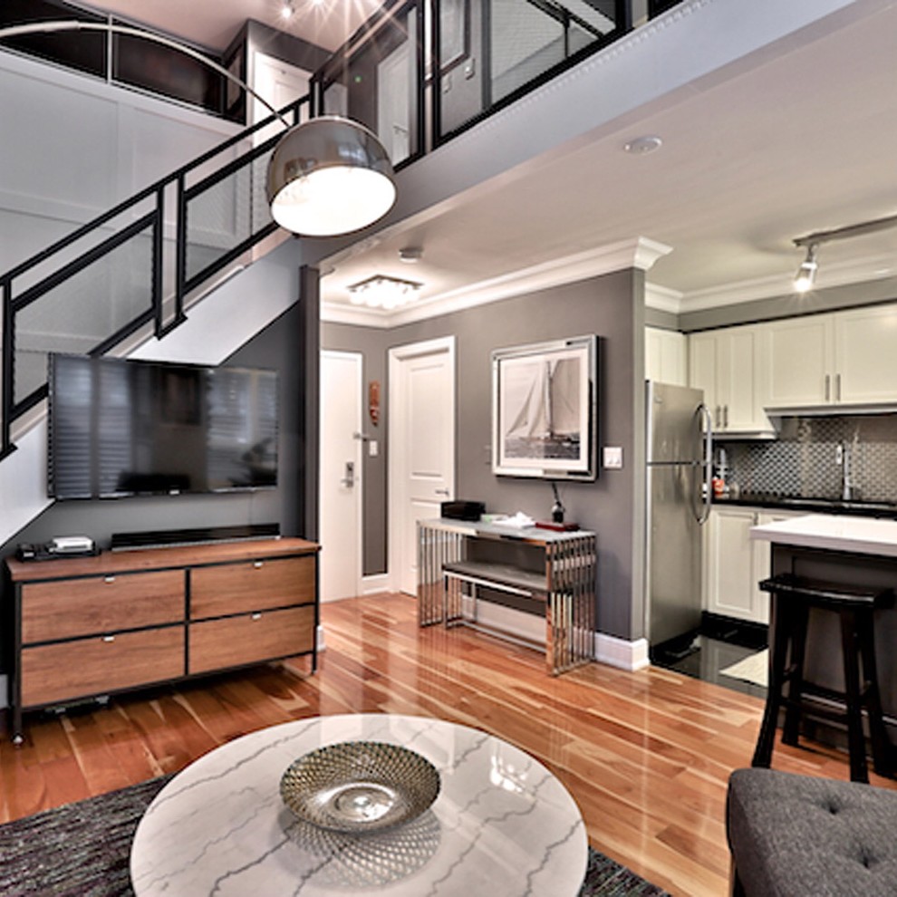 This is an example of a small transitional loft-style living room in Toronto with grey walls, light hardwood floors, no fireplace, a wall-mounted tv and beige floor.