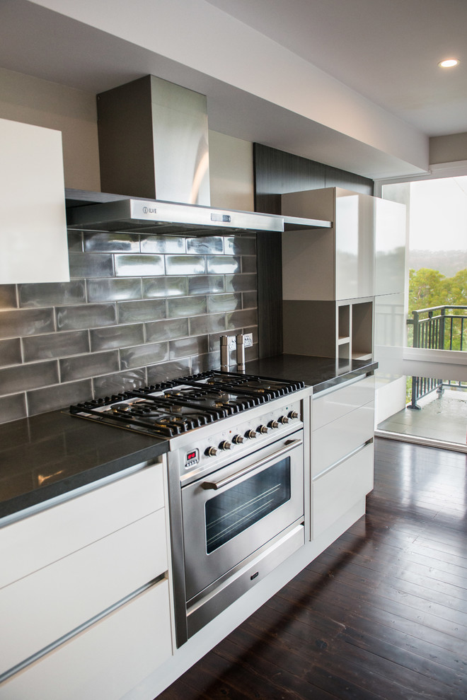 Large contemporary l-shaped eat-in kitchen in Sydney with a drop-in sink, wood benchtops, black splashback, ceramic splashback, stainless steel appliances, dark hardwood floors, with island, flat-panel cabinets, white cabinets and white benchtop.