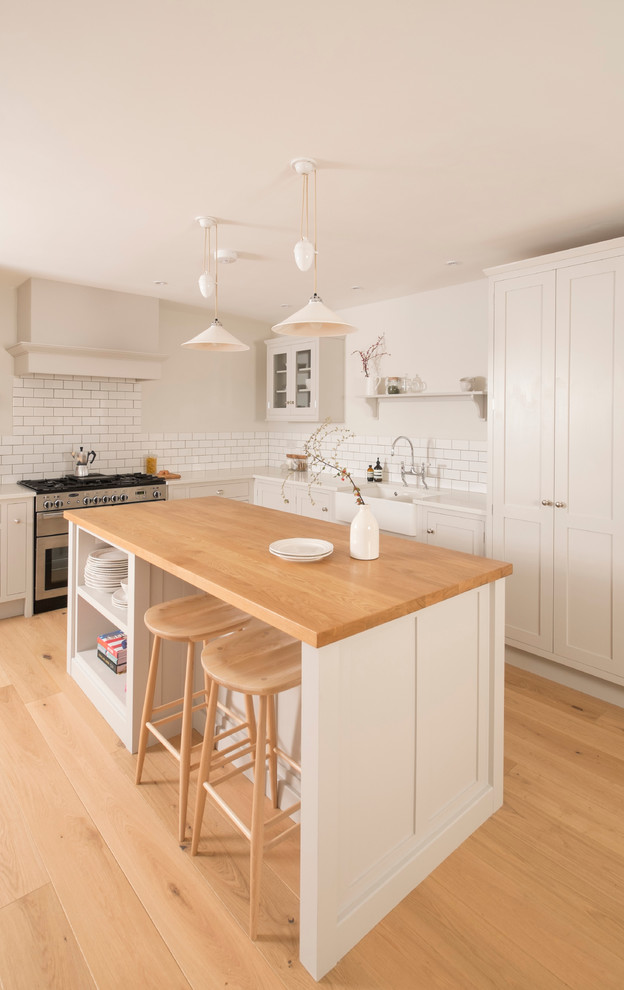 Design ideas for a mid-sized traditional l-shaped open plan kitchen in Cardiff with a farmhouse sink, shaker cabinets, white cabinets, quartzite benchtops, white splashback, subway tile splashback, stainless steel appliances, medium hardwood floors and with island.