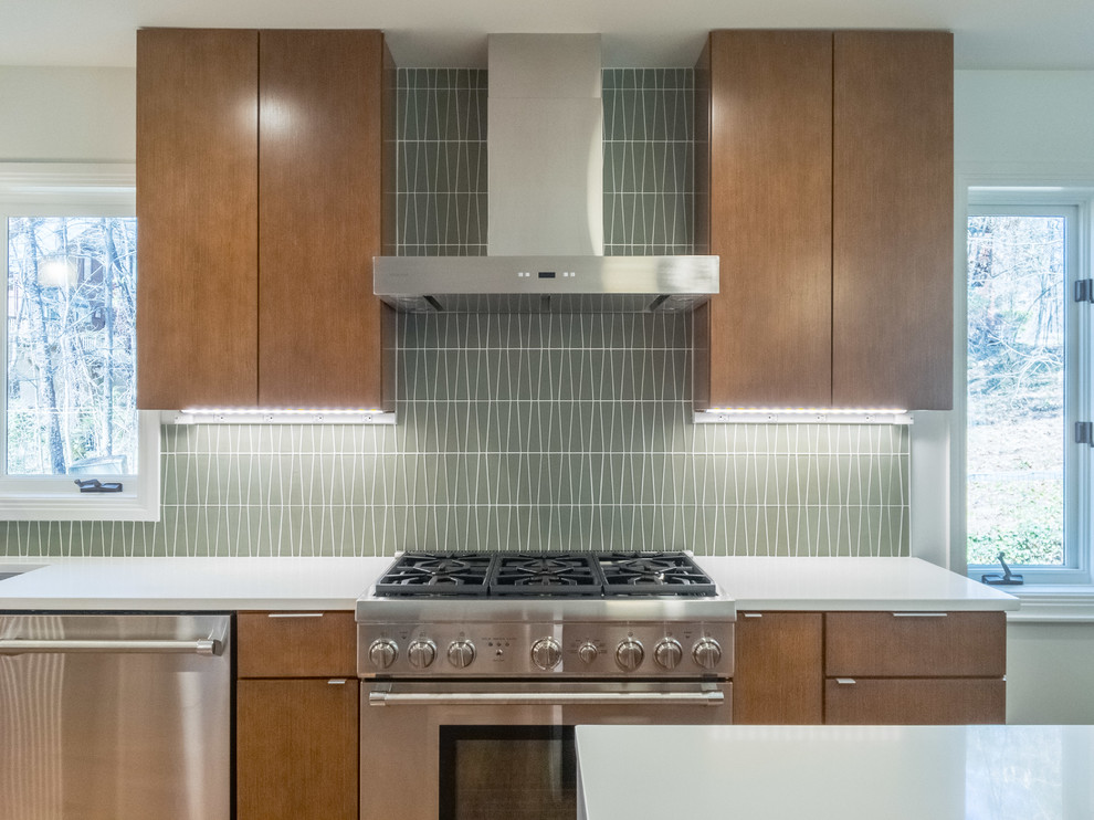 This is an example of a large midcentury l-shaped open plan kitchen in Raleigh with an undermount sink, flat-panel cabinets, medium wood cabinets, quartz benchtops, green splashback, glass tile splashback, stainless steel appliances, medium hardwood floors and with island.