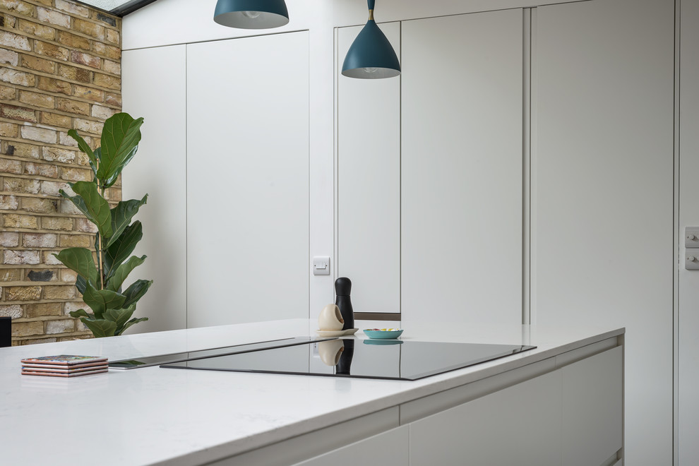 Inspiration for a mid-sized contemporary eat-in kitchen in London with an integrated sink, flat-panel cabinets, white cabinets, quartzite benchtops, white splashback, brick splashback, stainless steel appliances, concrete floors, with island and grey floor.