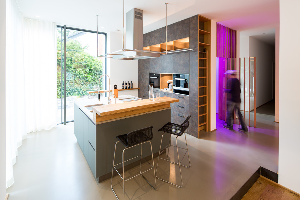 Large contemporary open plan kitchen in Bremen with a double-bowl sink, flat-panel cabinets, grey cabinets, wood benchtops, with island and black appliances.