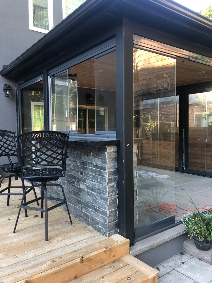 This is an example of a large contemporary backyard verandah in Toronto with an outdoor kitchen, concrete pavers and a roof extension.