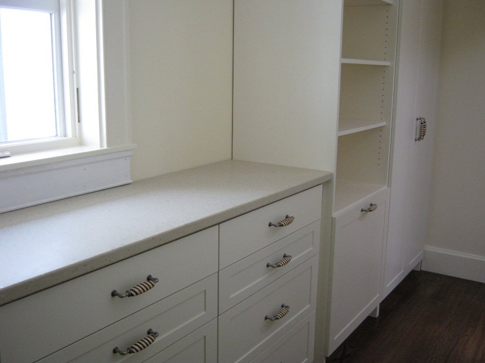Small contemporary gender-neutral walk-in wardrobe in Other with glass-front cabinets, white cabinets and dark hardwood floors.