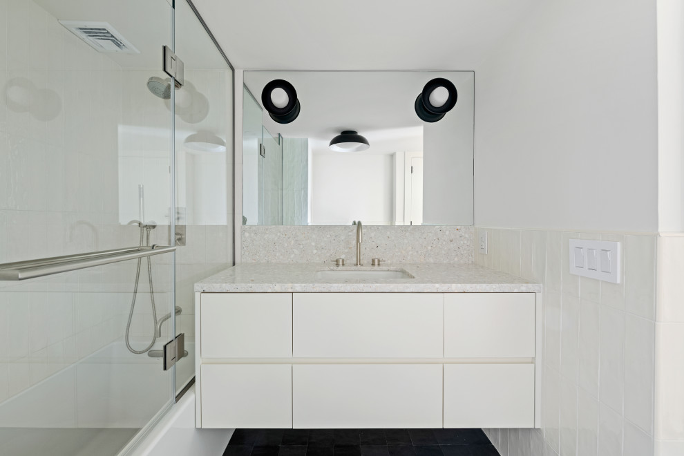 Inspiration for a mid-sized modern white tile and ceramic tile ceramic tile, black floor and single-sink bathroom remodel in New York with flat-panel cabinets, white cabinets, a wall-mount toilet, white walls, a drop-in sink, terrazzo countertops, a hinged shower door, beige countertops and a floating vanity