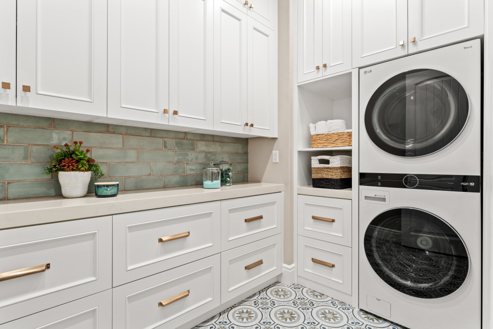 Design ideas for a traditional l-shaped separated utility room in Orange County with white cabinets, engineered stone countertops, green splashback, porcelain splashback, porcelain flooring, a stacked washer and dryer, recessed-panel cabinets, beige walls, multi-coloured floors and beige worktops.