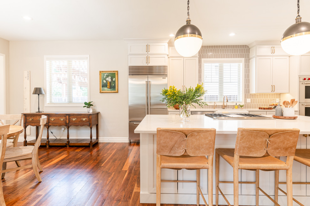 Large transitional l-shaped dark wood floor and brown floor open concept kitchen photo in Denver with a farmhouse sink, shaker cabinets, beige cabinets, quartz countertops, beige backsplash, ceramic backsplash, stainless steel appliances, an island and white countertops