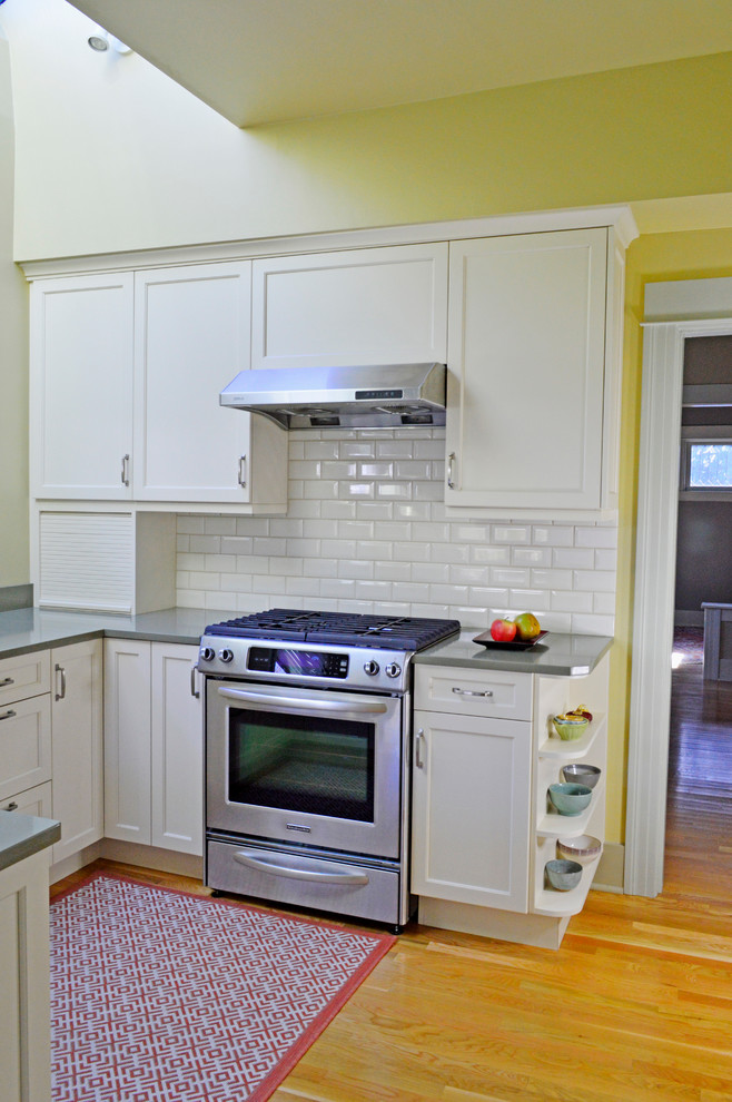 Example of a mid-sized transitional light wood floor enclosed kitchen design in Seattle with an undermount sink, recessed-panel cabinets, white cabinets, quartz countertops, white backsplash, subway tile backsplash, stainless steel appliances and a peninsula
