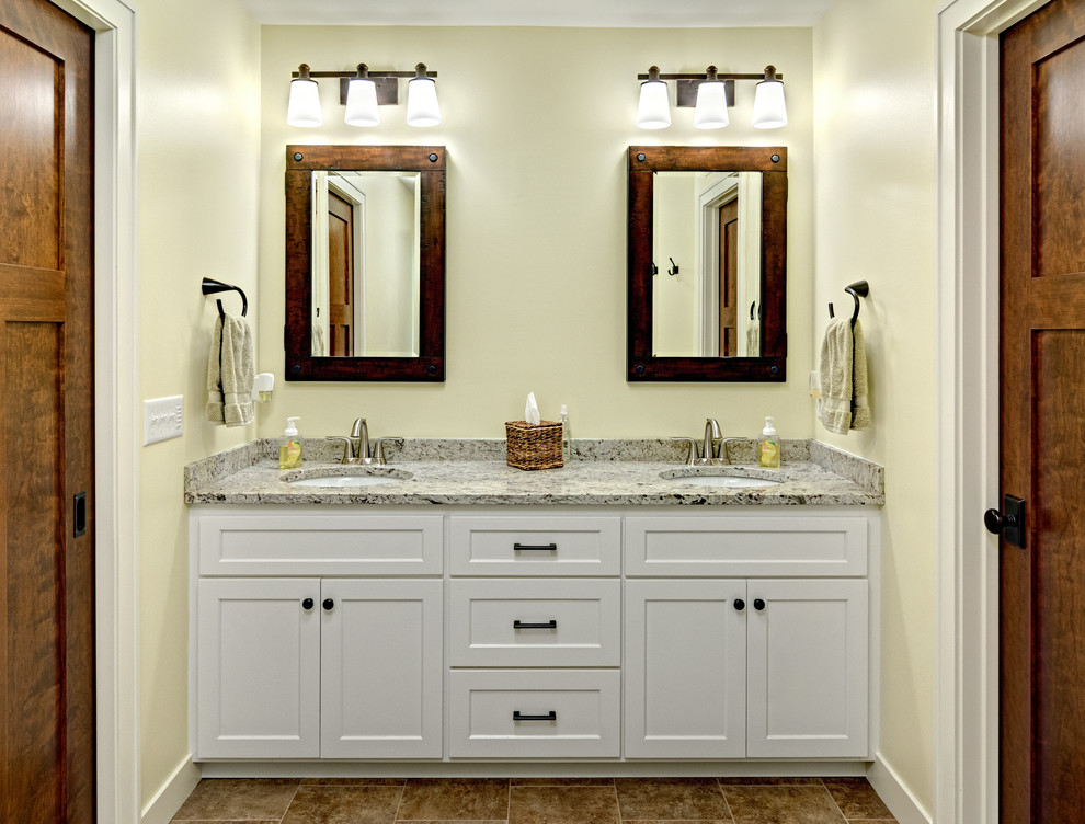 Mid-sized arts and crafts master bathroom in Minneapolis with shaker cabinets, white cabinets, a corner shower, yellow walls, porcelain floors, an undermount sink, granite benchtops, brown floor, a hinged shower door and multi-coloured benchtops.