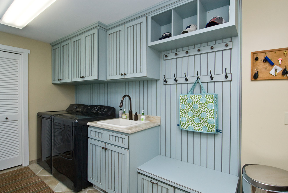 This is an example of a mid-sized traditional single-wall utility room in Other with a drop-in sink, blue cabinets, granite benchtops, beige walls, porcelain floors, a side-by-side washer and dryer, beige floor, beige benchtop and recessed-panel cabinets.