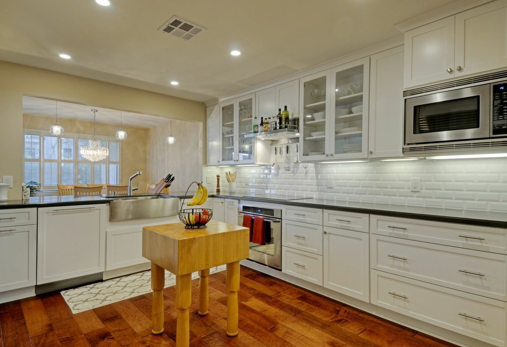 Inspiration for a mid-sized transitional galley medium tone wood floor open concept kitchen remodel with a farmhouse sink, shaker cabinets, white cabinets, quartz countertops, white backsplash, ceramic backsplash, stainless steel appliances and no island