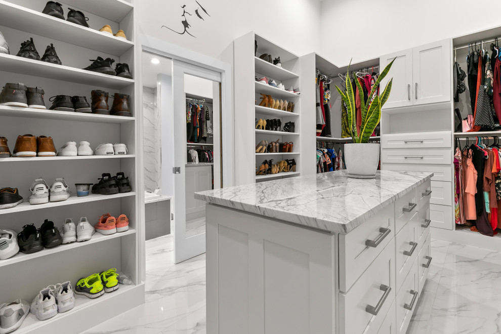 This is an example of a beach style gender-neutral walk-in wardrobe in Jacksonville with shaker cabinets, white cabinets, marble floors and white floor.