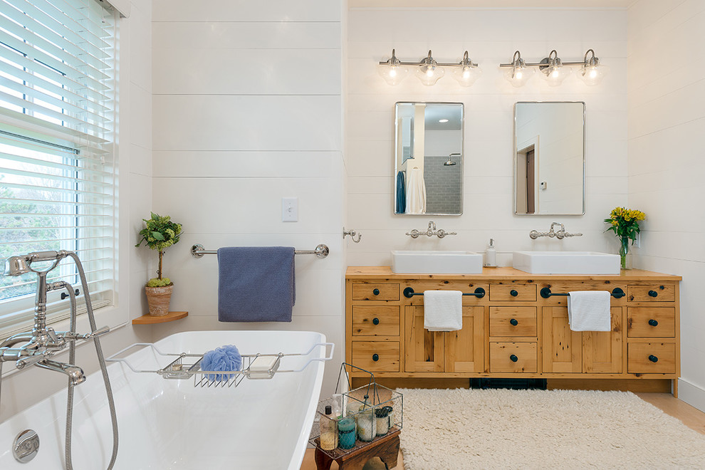 Design ideas for a large country master bathroom in Charlotte with shaker cabinets, distressed cabinets, a freestanding tub, light hardwood floors, a vessel sink, wood benchtops, white walls and brown benchtops.