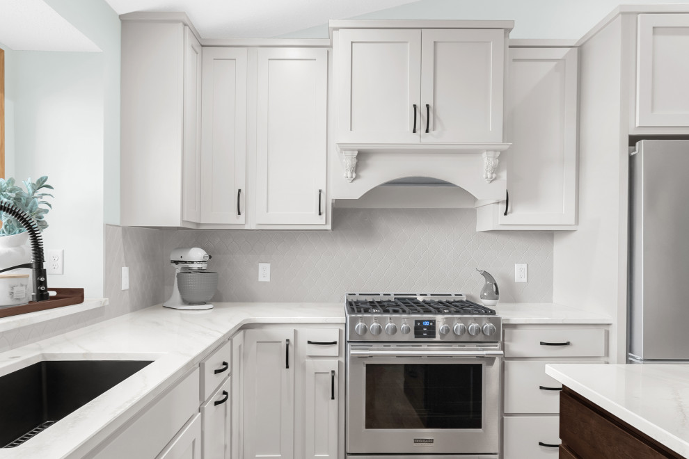 Example of a mid-sized transitional l-shaped light wood floor and beige floor kitchen design in Minneapolis with an undermount sink, shaker cabinets, white cabinets, quartz countertops, white backsplash, ceramic backsplash, stainless steel appliances, an island and white countertops