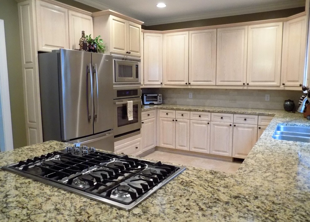 Large transitional u-shaped porcelain tile kitchen photo in Atlanta with a triple-bowl sink, raised-panel cabinets, light wood cabinets, granite countertops, beige backsplash, stone tile backsplash, stainless steel appliances and a peninsula
