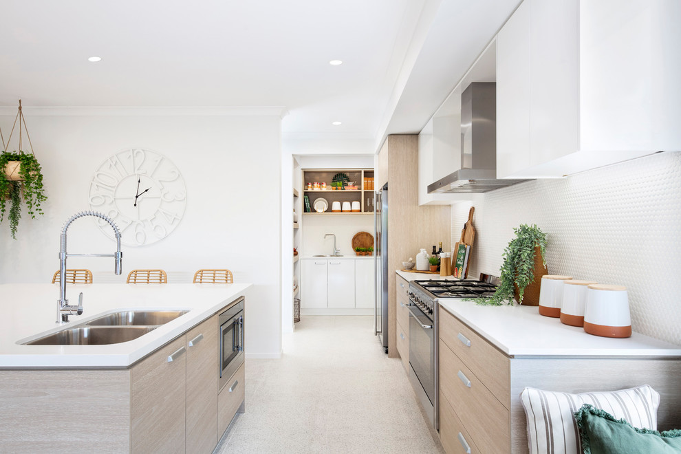 Photo of a beach style galley eat-in kitchen in Brisbane with a double-bowl sink, flat-panel cabinets, medium wood cabinets, white splashback, mosaic tile splashback, stainless steel appliances, with island, beige floor and white benchtop.