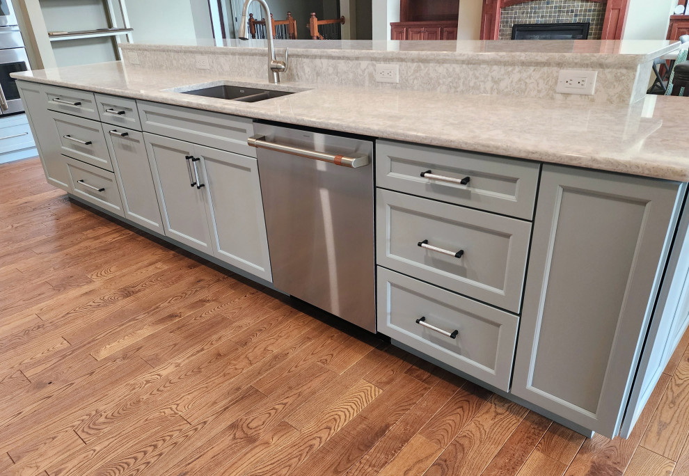 Open concept kitchen - mid-sized transitional medium tone wood floor and brown floor open concept kitchen idea with an undermount sink, shaker cabinets, quartz countertops, white backsplash, quartz backsplash, stainless steel appliances, an island and white countertops