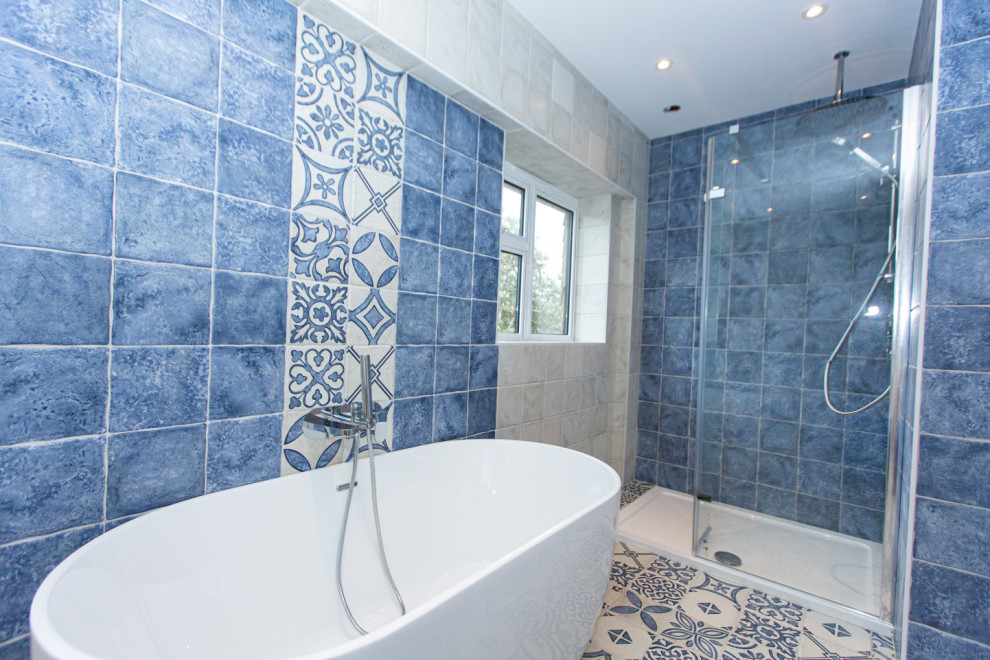 Large mediterranean ensuite bathroom in Sussex with medium wood cabinets, a freestanding bath, a walk-in shower, a one-piece toilet, blue tiles, ceramic tiles, white walls, wooden worktops, multi-coloured floors, a hinged door, a feature wall, double sinks and a freestanding vanity unit.