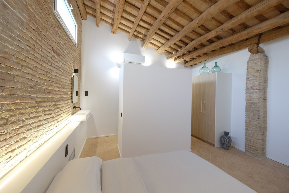 Mid-sized country guest bedroom in Barcelona with white walls, terra-cotta floors, no fireplace, beige floor and brick walls.