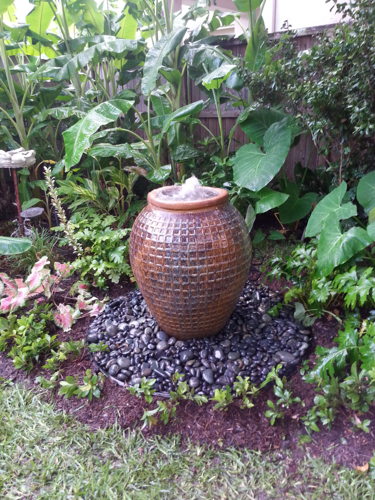 Ejemplo de jardín tropical en patio delantero con jardín francés, fuente y piedra decorativa