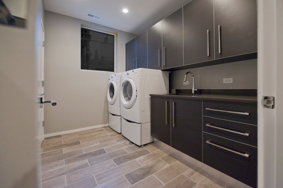 Photo of a mid-sized modern single-wall dedicated laundry room in Chicago with an undermount sink, grey cabinets, quartz benchtops, grey walls, porcelain floors and a side-by-side washer and dryer.