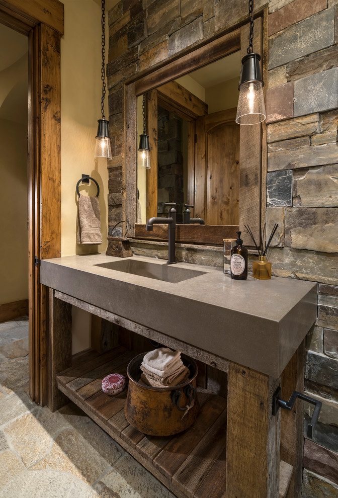 Photo of an expansive country powder room in Salt Lake City with open cabinets, medium wood cabinets, brown tile, gray tile, stone tile, yellow walls, an integrated sink, grey floor and grey benchtops.