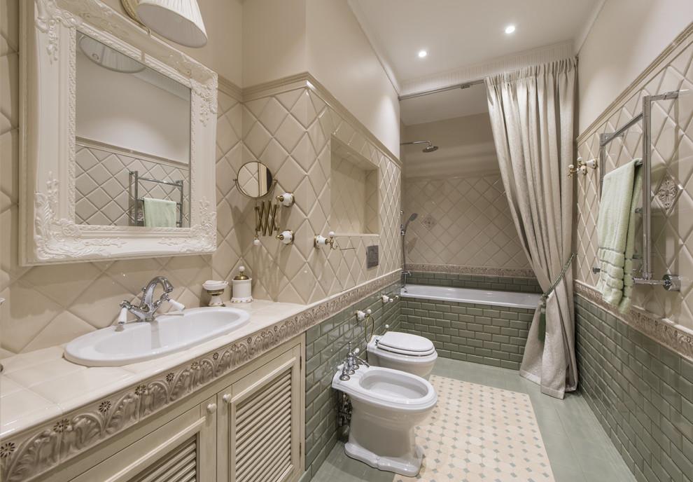 Design ideas for a traditional master bathroom in Moscow with a drop-in tub, green tile, beige tile, a drop-in sink, louvered cabinets, beige cabinets, a bidet, subway tile, beige walls, tile benchtops, green floor, a shower curtain and beige benchtops.