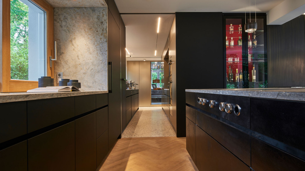 Modelo de cocina actual con puertas de armario negras, suelo de madera clara y encimeras beige