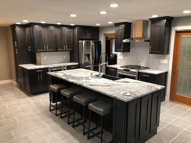 Inspiration for a mid-sized transitional l-shaped porcelain tile and gray floor open concept kitchen remodel in Cincinnati with a farmhouse sink, recessed-panel cabinets, dark wood cabinets, granite countertops, white backsplash, subway tile backsplash, stainless steel appliances, an island and gray countertops