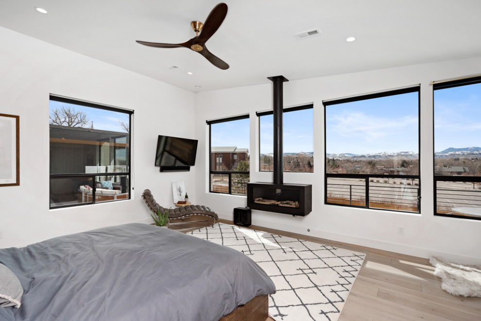 Modern master bedroom in Denver with white walls, light hardwood floors, a hanging fireplace and a metal fireplace surround.