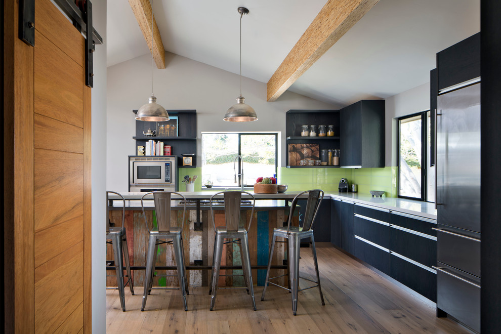 Mid-sized transitional l-shaped light wood floor eat-in kitchen photo in San Diego with flat-panel cabinets, black cabinets, stainless steel appliances, solid surface countertops, green backsplash and subway tile backsplash