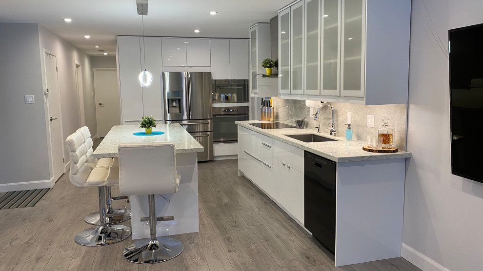 Photo of a mid-sized contemporary galley open plan kitchen in Toronto with an undermount sink, glass-front cabinets, white cabinets, quartz benchtops, grey splashback, porcelain splashback, stainless steel appliances, laminate floors, with island, grey floor and multi-coloured benchtop.