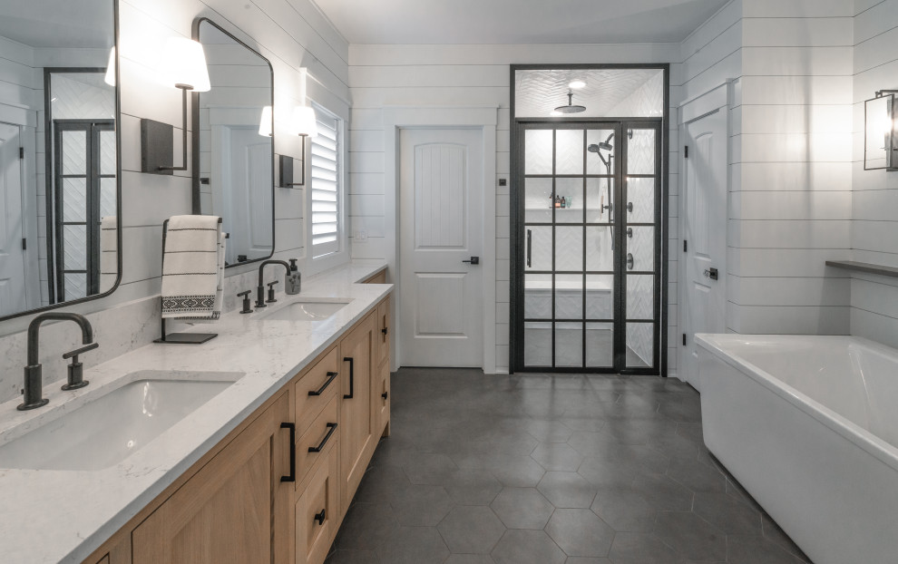 Photo of a large modern ensuite bathroom in Milwaukee with recessed-panel cabinets, light wood cabinets, a freestanding bath, a built-in shower, white tiles, ceramic tiles, white walls, ceramic flooring, a submerged sink, quartz worktops, grey floors, a hinged door, white worktops, an enclosed toilet, double sinks, a freestanding vanity unit and tongue and groove walls.
